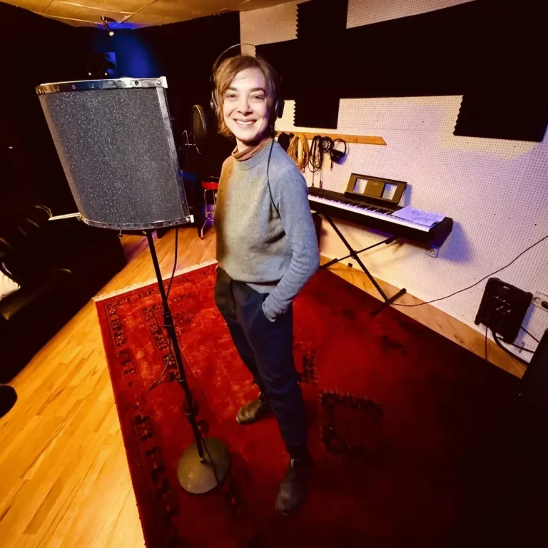 Sprecher-Casting in Hamburg Person steht neben einem Mikrofon in einem Musikstudio mit Klavier im Hintergrund.