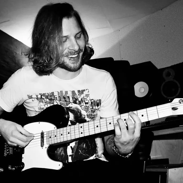 Songwriting in Hamburg Lächelnder Mann spielt Gitarre in einem Musikstudio.