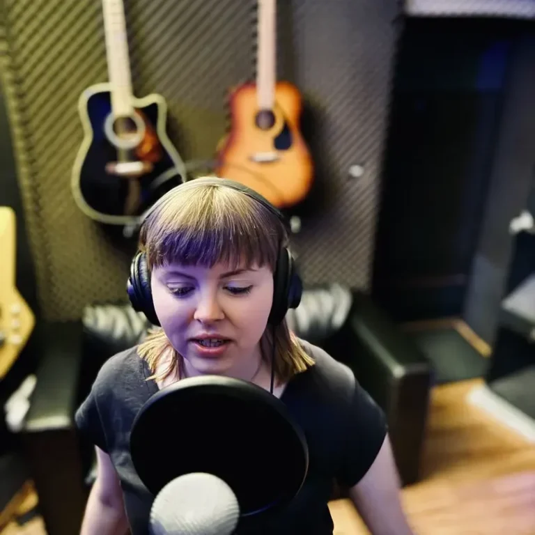 Vocal Tuning in Hamburg Frau mit Kopfhörern singt in einem Tonstudio vor einem Mikrofon. Akustische Gitarren im Hintergrund.