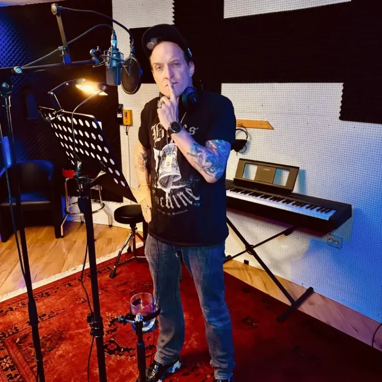 Sprachaufnahmen / Voice Over aufnehmen Hamburg Mann im Aufnahmestudio mit Mikrofon, Gitarrenständer und Klavier im Hintergrund.